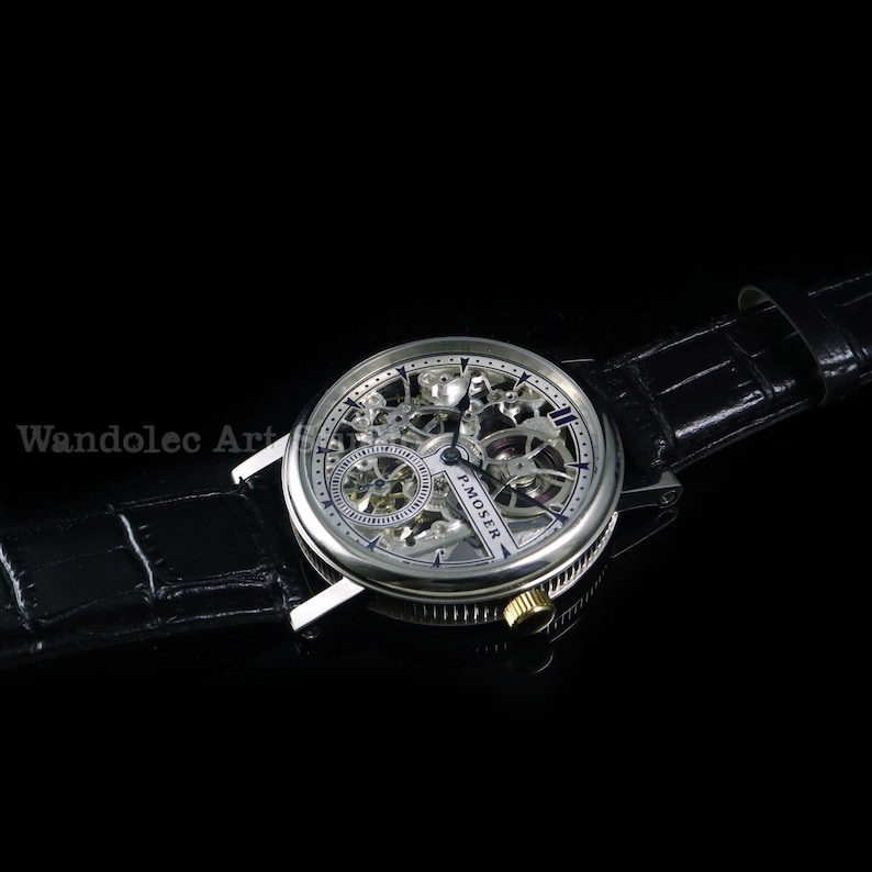 May include: A silver skeleton watch with a black leather band. The watch face reveals the intricate inner workings of the timepiece. The watch has a round face with a silver bezel and a black leather strap. The watch is a luxury item.