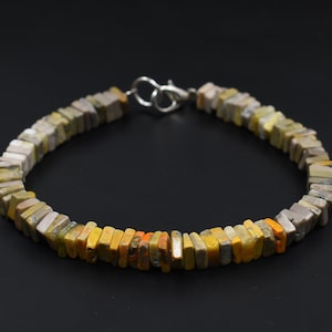 May include: A bracelet made of yellow, brown, and gray square-shaped stones. The bracelet has a silver clasp.