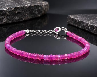 May include: A bracelet composed of small, round, vibrant pink beads with a subtle iridescent sheen. The piece features a silver-toned metal chain extender and a circular spring ring clasp, providing a secure closure for the delicate strand.