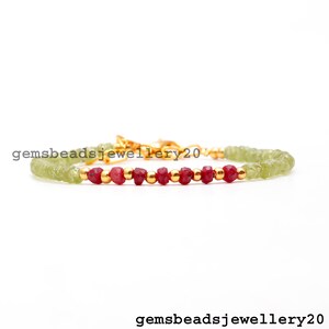 Puede incluir: Un brazalete delicado hecho con cuentas de piedras preciosas verdes y rojas. El brazalete tiene un cierre dorado y está enhebrado en una cadena dorada.