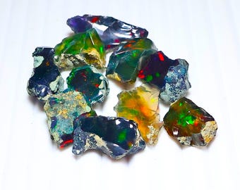 May include: A collection of rough opal gemstones. The opals display a variety of colors, including green, red, blue, and yellow, with flashes of iridescence. The stones have a natural, unpolished appearance.