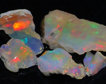 May include: A collection of raw opal gemstones. The opals display a variety of colors, including iridescent flashes of red, orange, green, and blue. The rough stones have a natural, unpolished appearance, showcasing their unique textures.