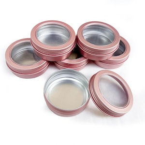 May include: A set of seven rose gold metal containers with clear lids. The containers are round and have a screw-on lid.