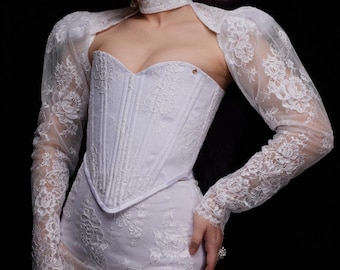 May include: A white lace corset with a sweetheart neckline and long sleeves. The corset has a boned structure and a fitted silhouette. The sleeves are sheer and have a delicate floral pattern.
