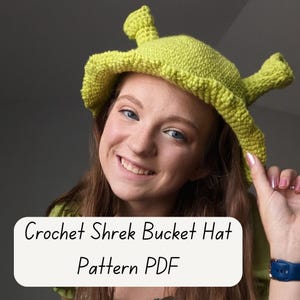 May include: A lime green crochet bucket hat with Shrek-like features. The hat has a wide brim and two horn-like protrusions. The text "Crochet Shrek Bucket Hat Pattern PDF" is displayed on a white background.