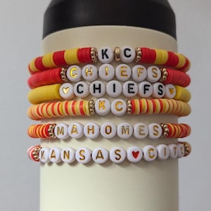 Op de afbeelding: Een set van vijf armbanden met rode, gele en witte kralen. De kralen spellen "KC Chiefs", "KC Chiefs", "Mahomes" en "Kansas City".