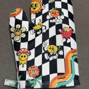 May include: Oven mitt with a black and white checkered pattern. The mitt features cartoon illustrations of a smiling sun, banana, orange, lemon, mushroom, flower, and french fries. A rainbow design is on the side.