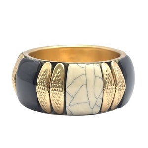 May include: A wide, gold-lined bangle bracelet. The bracelet features alternating sections of black, cream-colored, and gold-toned accents. The cream-colored sections have a cracked pattern. The gold sections have a textured design.