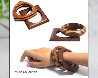 May include: Two wooden bangles with a striped pattern. The bangles are stacked on top of each other and are shown on a white background. The bangles are part of the Muse Collection by Pure Hands Studio.