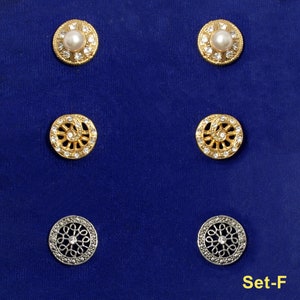May include: Set of six decorative buttons, two gold with clear rhinestones, two gold with a clear rhinestone center and a decorative design, and two silver with a clear rhinestone center and a decorative design. The buttons are arranged in two rows of three on a blue background. The text "Set-F" is in the bottom right corner of the image.