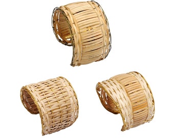 Puede incluir: Tres anillos para servilletas de bambú tejido con un borde de alambre dorado. Los anillos están en diferentes posiciones, mostrando el patrón tejido.
