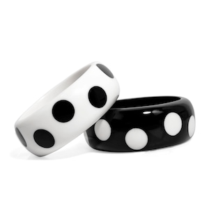 May include: Two chunky bangles, one white with black polka dots and the other black with white polka dots, are displayed against a white background. The bracelets are made of a glossy material and have a rounded shape. Fashion jewelry.