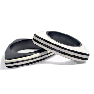 May include: Two black and white striped bangle bracelets with a triangular shape.