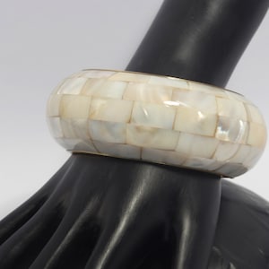 Könnte beinhalten: Ein weißes und goldenes Armreif-Armband aus eingelegten Perlmutt-Fliesen.