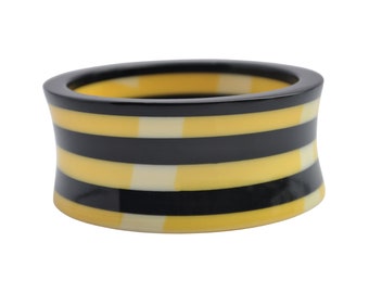 May include: A yellow and black striped bangle bracelet made of resin. The bracelet is wide and has a slightly curved shape.