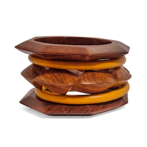 May include: A set of four wooden bangles, two are brown and two are yellow. The brown bangles are carved with a geometric pattern. The yellow bangles are smooth.