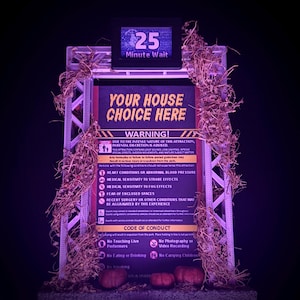 May include: A sign for a haunted house attraction with the text "Your House Choice Here" and a warning about intense content. A digital display shows "25 Minute Wait." The sign is framed with metal and decorated with dried foliage. Pumpkins are at the base.