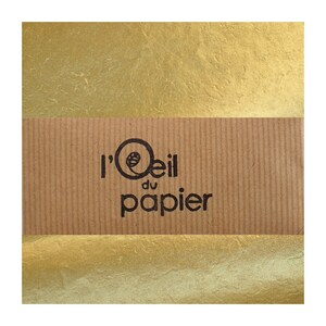 Peut inclure: Gros plan sur un papier doré avec une surface texturée. Une bande de carton marron avec le texte "l'Oeil du papier" est centrée horizontalement sur le papier.