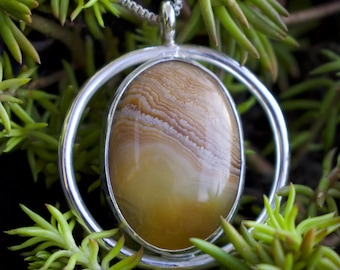 May include: A silver pendant necklace with a brown and white agate stone set in a silver circle. The stone has a swirling pattern.