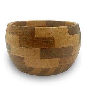 May include: A wooden bowl with a unique geometric pattern made from different shades of wood. The bowl is round and has a smooth, polished finish.