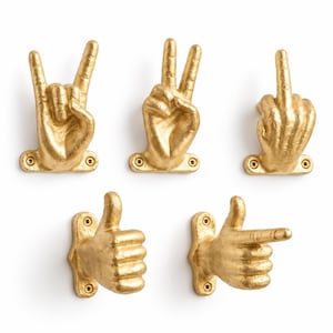 May include: A set of five gold-colored wall hooks shaped like human hands in various gestures, including a rock-on sign, a peace sign, a middle finger, a thumbs-up, and a pointing finger. Each hook features a mounting plate with two screw holes.