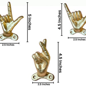 May include: Three gold-colored hand-shaped wall hooks. The largest hook is 5 inches tall and 2.5 inches wide. The other two hooks are 4.5 inches tall and 2.5 inches wide. Each hook has a mounting plate with two holes.