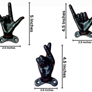 May include: Set of three black cast iron hand-shaped wall hooks. The hooks are in the shape of hand gestures, including "I love you", "hang loose", and crossed fingers. Each hook is approximately 2.5 inches wide and between 4.5 and 5 inches tall.