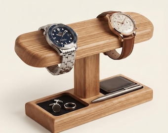 May include: A wooden watch stand with a horizontal bar holding two wristwatches, one with a blue face and silver band, the other with a white face and brown leather strap. The base features two recessed trays containing cufflinks, a ring, and a pen.