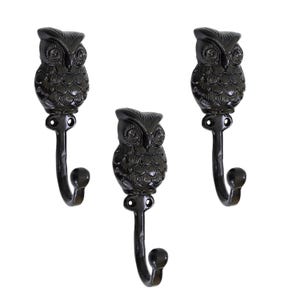 Może przedstawiać: Trzy ciemnobrązowe haczyki ścienne w kształcie sowy. Każdy haczyk ma szczegółową figurkę sowy na zakrzywionym haczyku z zaokrąglonym końcem. Haczyki są przeznaczone do wieszania przedmiotów.