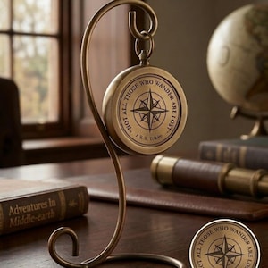 Könnte beinhalten: Ein Messingkompass mit dekorativem Ständer. Der Kompass hat ein nautisches Sterndesign und das Zitat "Not all those who wander are lost". Der Ständer ist ein geschwungenes, elegantes Design. Der Kompass ist ein Artikel im Vintage-Stil.