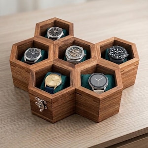May include: A hexagonal wooden watch storage box with six individual compartments, each containing a wristwatch resting on a dark teal cushion. The box features a natural wood grain finish and a silver metal latch on the front exterior panel.