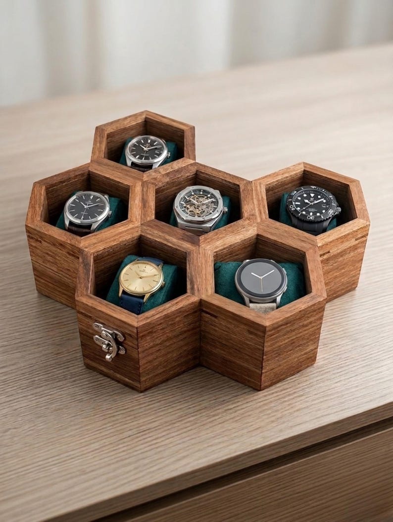 May include: A hexagonal wooden watch storage box with six individual compartments, each containing a wristwatch resting on a dark teal cushion. The box features a natural wood grain finish and a silver metal latch on the front exterior panel.