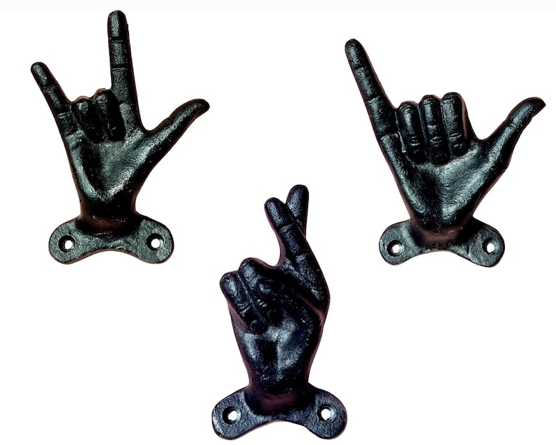 May include: Three black cast iron hand-shaped wall hooks. One hook forms the "I love you" sign, another the "hang loose" gesture, and the third has fingers crossed. Each hook has a mounting plate with two holes.