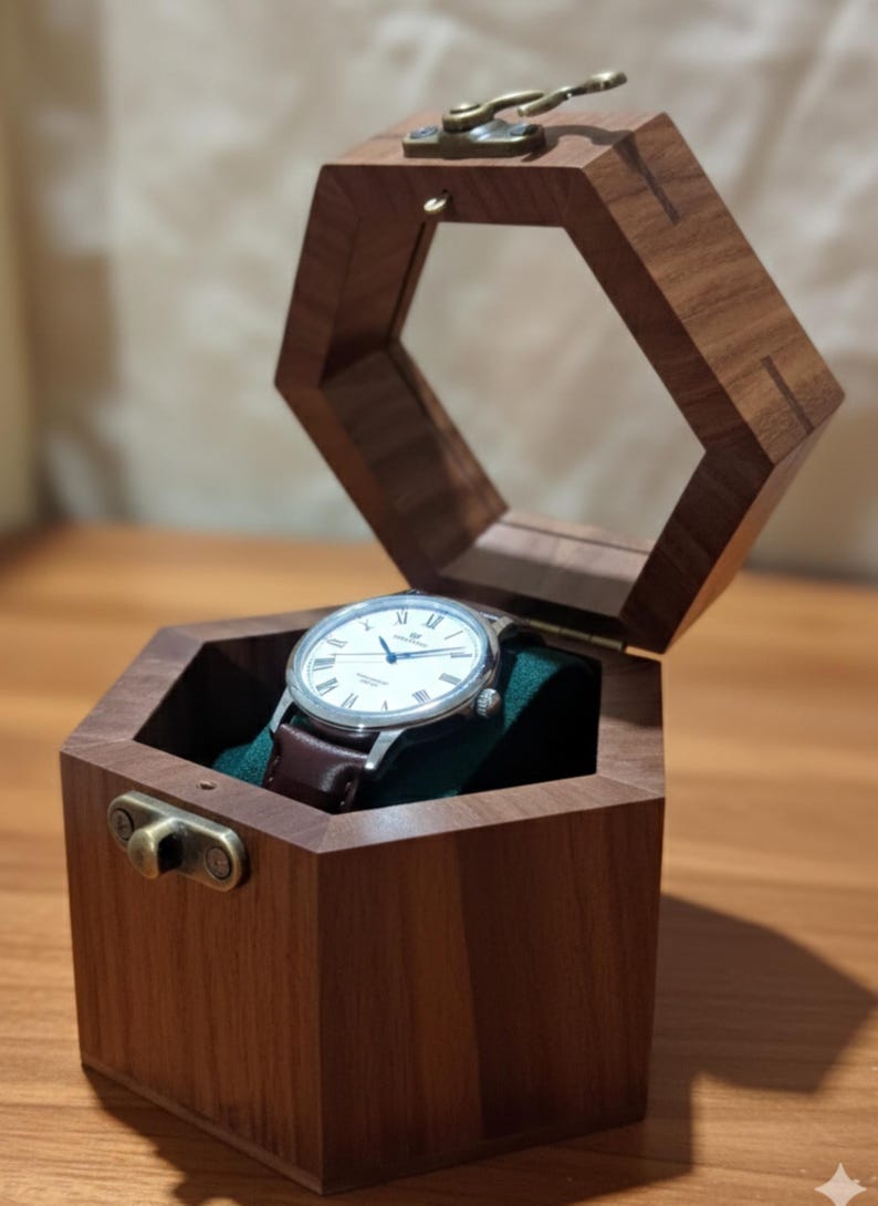 May include: A hexagonal wooden watch box with a hinged lid and brass latch, featuring a dark brown wood grain finish. Inside, a silver-cased wristwatch with a white dial and dark brown leather strap rests on a dark green velvet cushion.