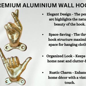May include: Gold-colored aluminum wall hooks shaped like hands, one with fingers crossed and the other with a shaka sign. The hooks are mounted on a white background and are labeled "PREMIUM ALUMINIUM WALL HOOK".