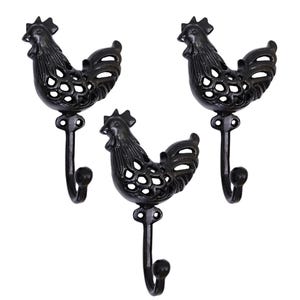 Może przedstawiać: Trzy czarne metalowe haczyki ścienne w kształcie koguta. Każdy haczyk ma szczegółowy wzór koguta z ażurowymi detalami i zakrzywionym haczykiem na dole. Haczyki są przeznaczone do wieszania przedmiotów i dodają dekoracyjnego akcentu.