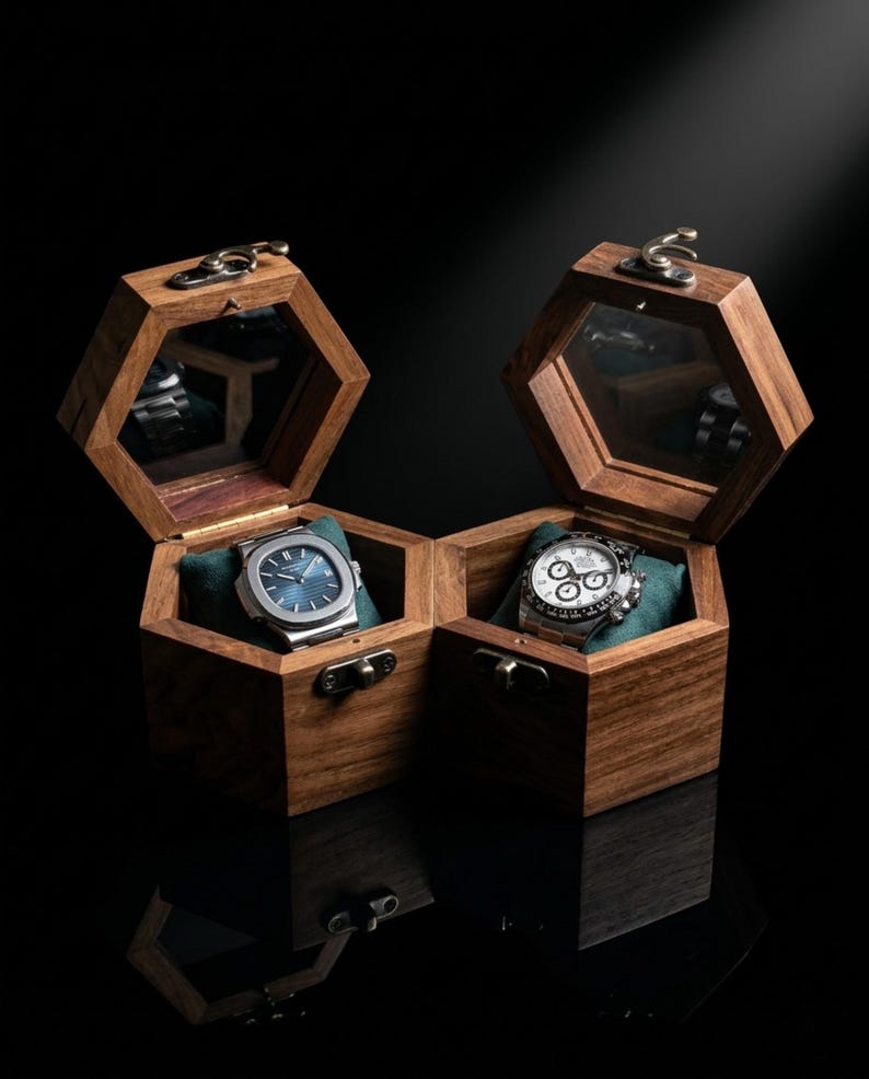 May include: Two hexagonal wooden watch boxes with hinged lids and brass-toned latches. Each box features a glass-topped lid, a dark green velvet cushion, and a silver-toned wristwatch. One watch has a blue dial, and the other has a white dial.
