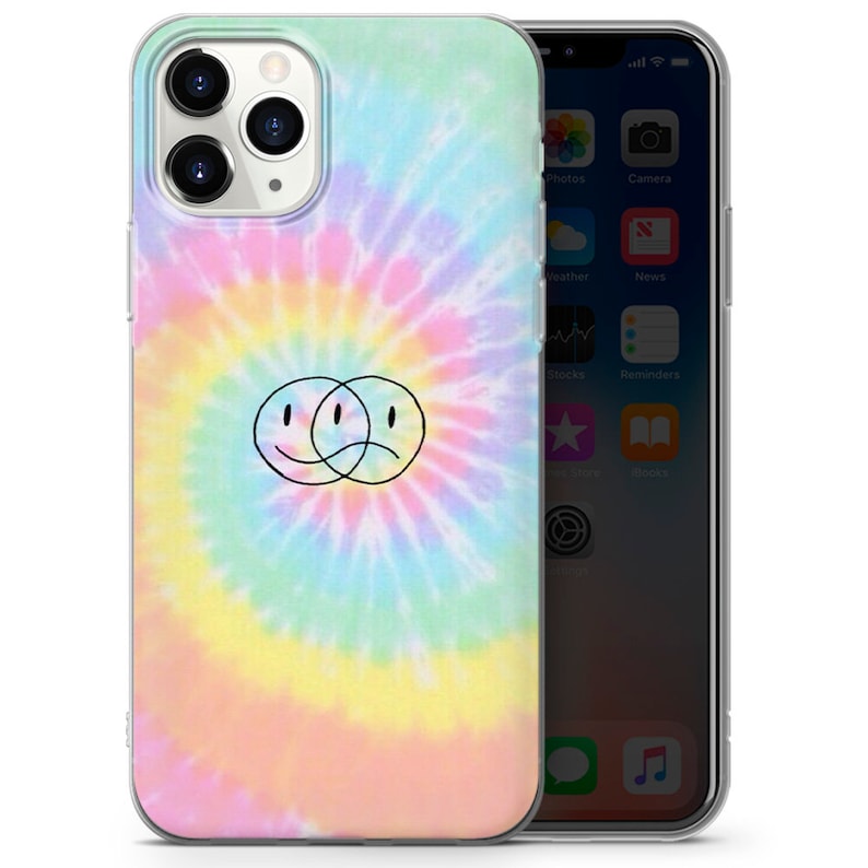 May include: A clear phone case with a tie-dye pattern in shades of pink, yellow, blue, and green. A black outline of two overlapping smiley faces, one smiling and one frowning, is centered on the case.