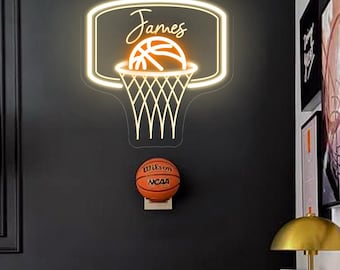 May include: A neon basketball hoop with the name "James" in a bedroom setting. Below the hoop is a basketball mounted on the wall. The room features a desk, chair, and artwork, creating a sports-themed decor.