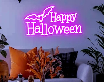 May include: A neon sign that reads "Happy Halloween" in bright pink, with a bat silhouette above the text. The sign is mounted on a wall above a gray sofa with orange and black pillows. Decorative bats are also on the wall.