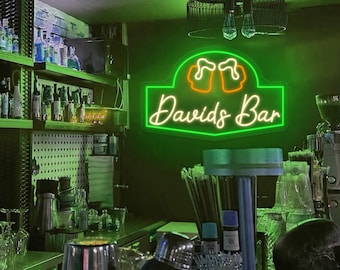 May include: A green neon sign with the text "David's Bar" in white neon lettering. Two orange neon beer mugs are above the text. The sign is mounted on a wall in a bar setting.