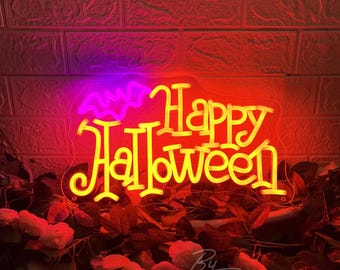 May include: A neon sign featuring the text Happy Halloween in bright yellow script, accompanied by a purple neon bat outline above the words. The sign is mounted on a clear acrylic backing and is illuminated against a textured brick wall.