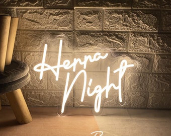 May include: A white neon sign that reads "Henna Night" in a script font. The sign is mounted on a clear backing and is illuminated against a textured brick wall. The words "By ZPL Neon Custom" are written below the sign.