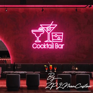May include: A neon sign with the words "Cocktail Bar" and three cocktail glasses in white against a dark pink wall. The sign is in a bar setting with seating and tables. The sign is made by ZP Neon Custom.