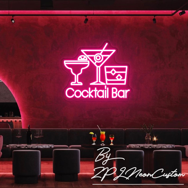May include: A neon sign with the words "Cocktail Bar" and three cocktail glasses in white against a dark pink wall. The sign is in a bar setting with seating and tables. The sign is made by ZP Neon Custom.