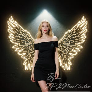 Könnte beinhalten: Eine Frau in einem schwarzen schulterfreien Kleid steht vor einer Neon-Lichtanzeige mit Engelsflügeln. Die Flügel sind in einer warmen, goldenen Farbe vor einem dunklen Hintergrund umrissen. Der Text "By ZPL Neon Custom" ist sichtbar.