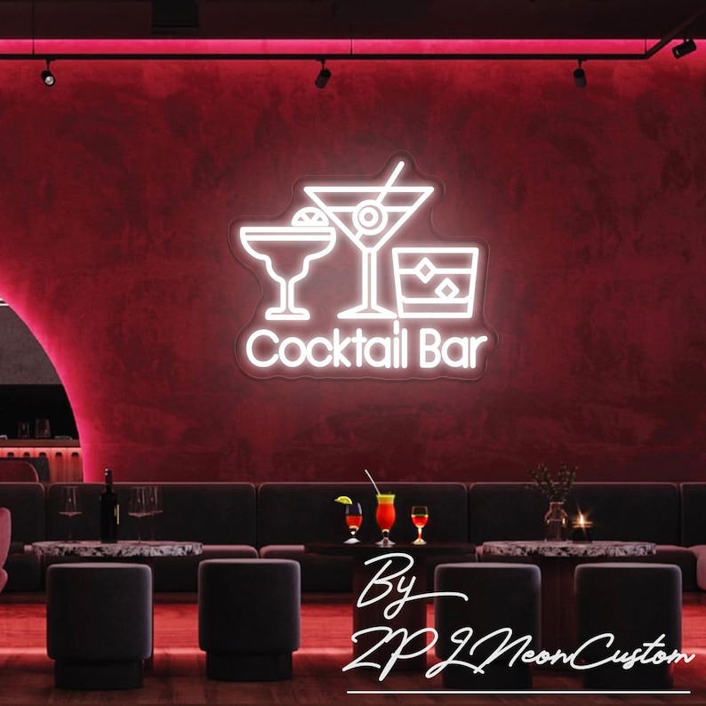 May include: A neon sign for a cocktail bar, featuring three drink glasses and the words "Cocktail Bar" in white. The sign is mounted on a dark red wall. The image also shows a bar setting with seating and tables.
