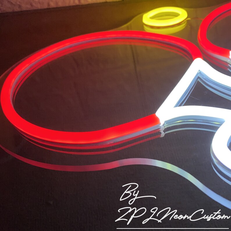 May include: Close-up of a neon sign with a red, white, and yellow color scheme. The sign is in the shape of a flower. The text "By ZP Neon Custom" is written in white cursive font.