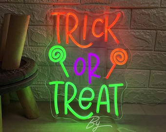 May include: A neon sign with the words "TRICK OR TREAT" in orange, green, and purple. The sign has a clear backing and features lollipop designs. The sign is for Halloween.