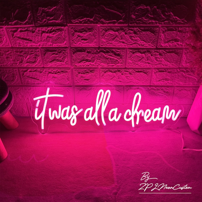 May include: A neon sign in a cursive font that reads "it was all a dream" in white against a pink background. The sign is illuminated, casting a pink glow. The words "By ZP Z Neon Custom" are at the bottom.